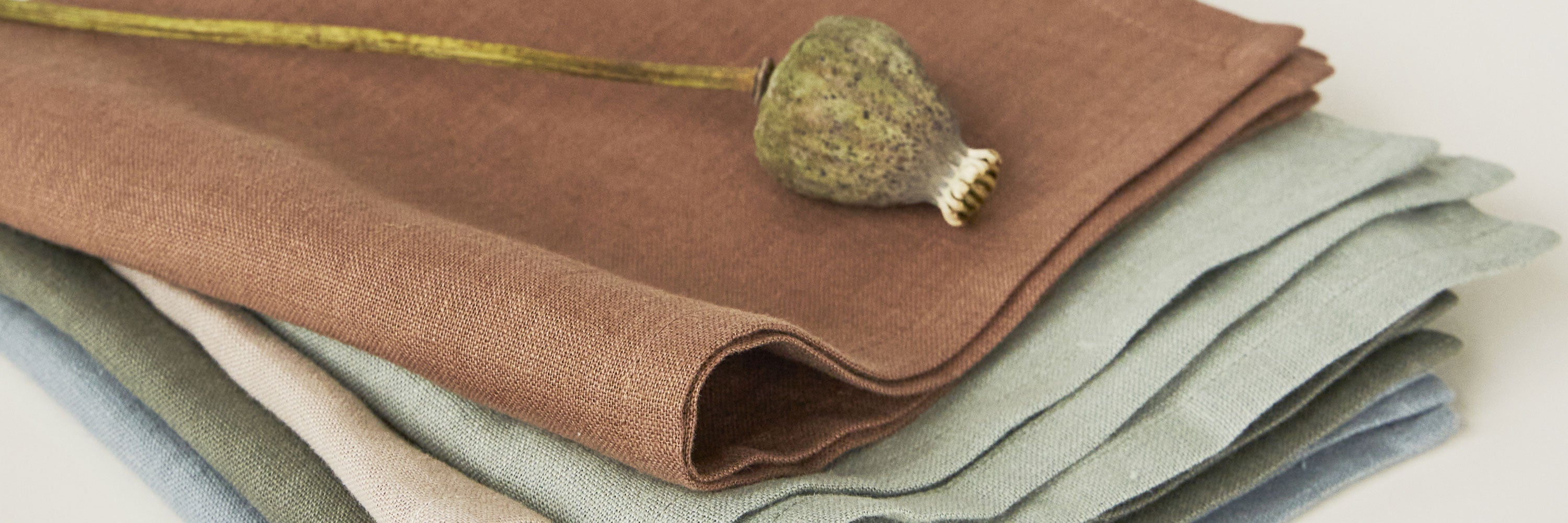 Folded natural table linens including tablecloths, napkins, placemats, and linen runners in neutral tones with handcrafted, custom-made feel.