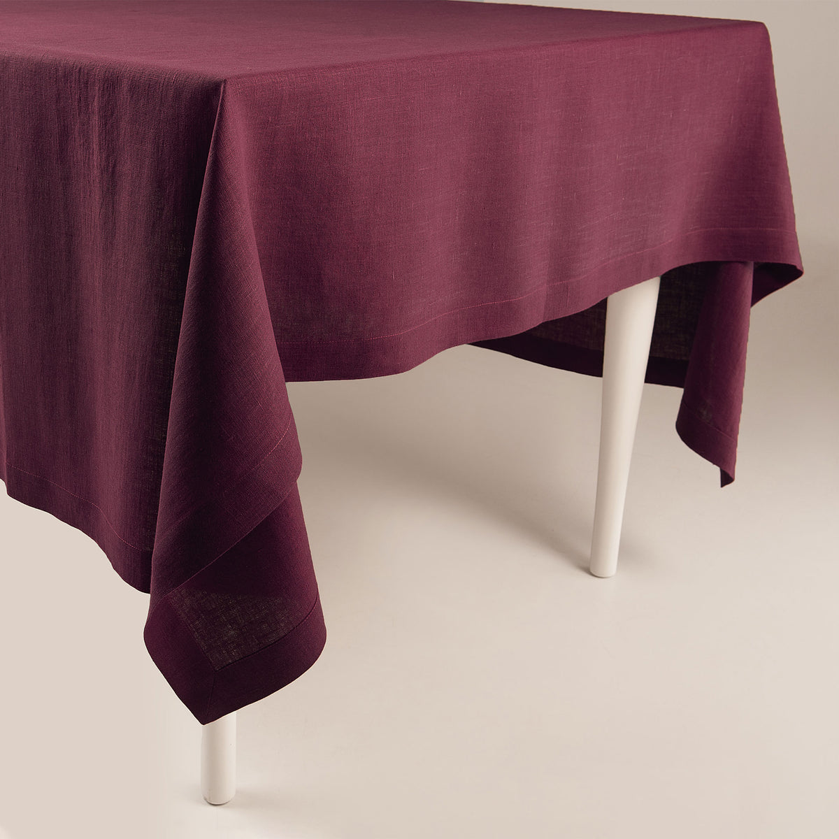 Deep Burgundy natural linen tablecloth draped over a table, showing handmade classic deep hems and mitered corners.